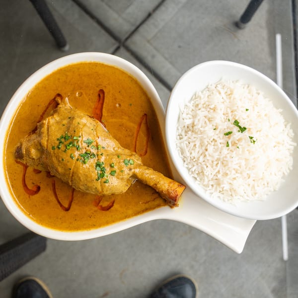 Lamb shank in a rich curry sauce with a side of white rice, garnished with herbs.