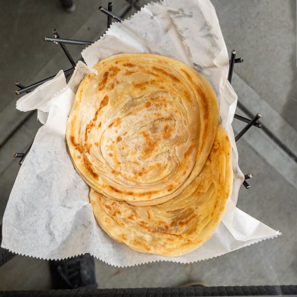 Two golden-brown, flaky paratha flatbreads served in a black wire basket lined with white paper.