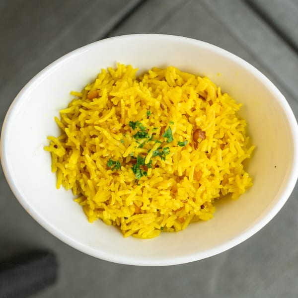 A white bowl filled with vibrant yellow rice, garnished with fresh green herbs.