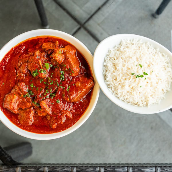 Overhead view of a bowl of red curry with meat and a side bowl of white rice.