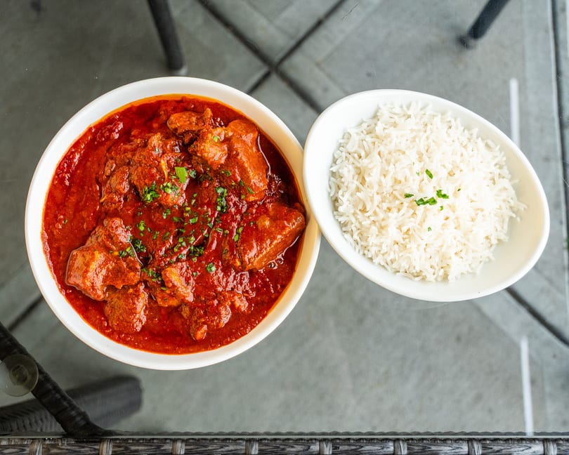 Overhead view of a bowl of red curry with meat and a side bowl of white rice.