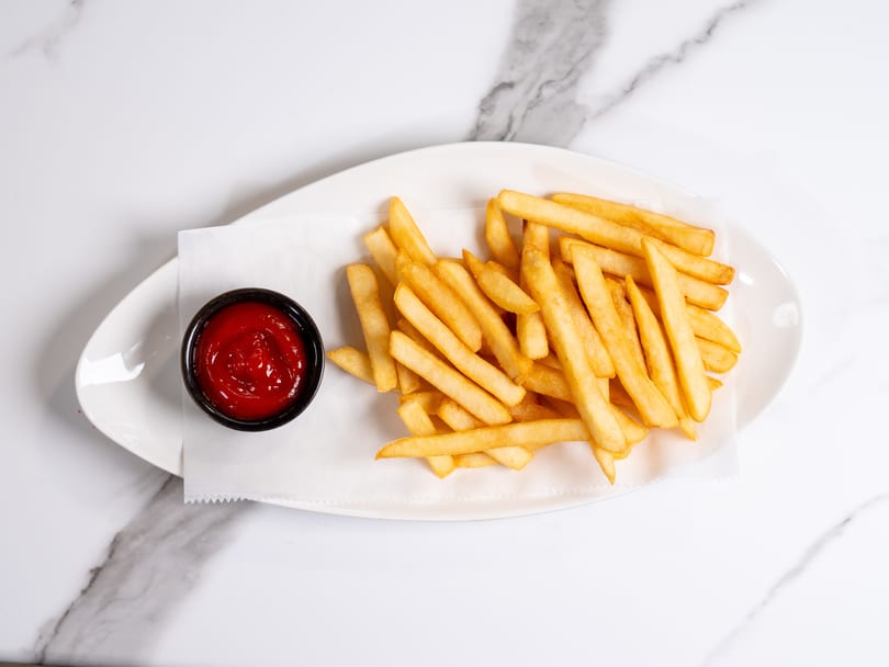Golden french fries on a white plate with a side of ketchup, on a marble surface.