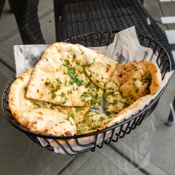 A black wire basket filled with warm, garlic naan bread, garnished with fresh parsley.