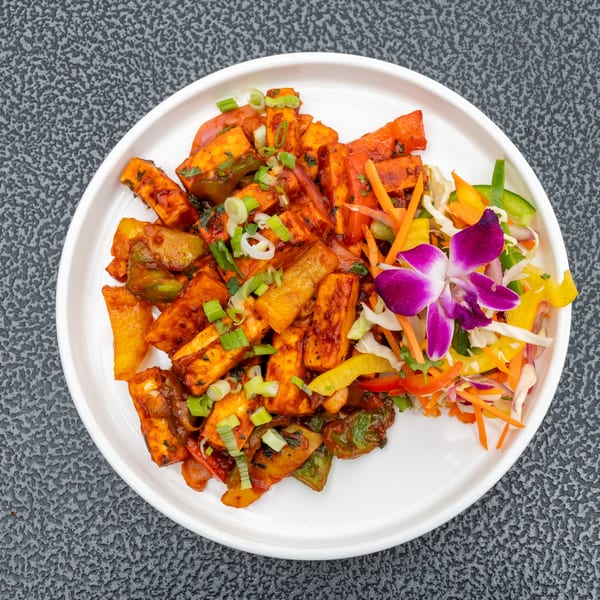 Chili Paneer, a spicy Indian dish with paneer, bell peppers, and onions, garnished with a purple orchid.
