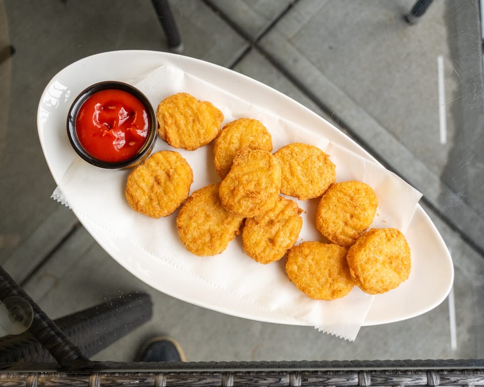 Golden-brown chicken nuggets with a side of ketchup on a white plate, viewed from above.