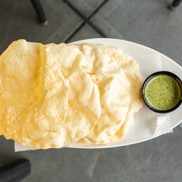 Crispy papadum crackers and a small bowl of green chutney on a white plate.