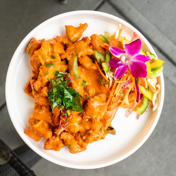 Orange curry dish with green herbs, dried chilis, and a side salad with an orchid garnish.