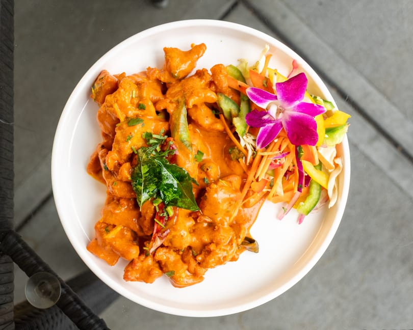 Orange curry dish with green herbs, dried chilis, and a side salad with an orchid garnish.