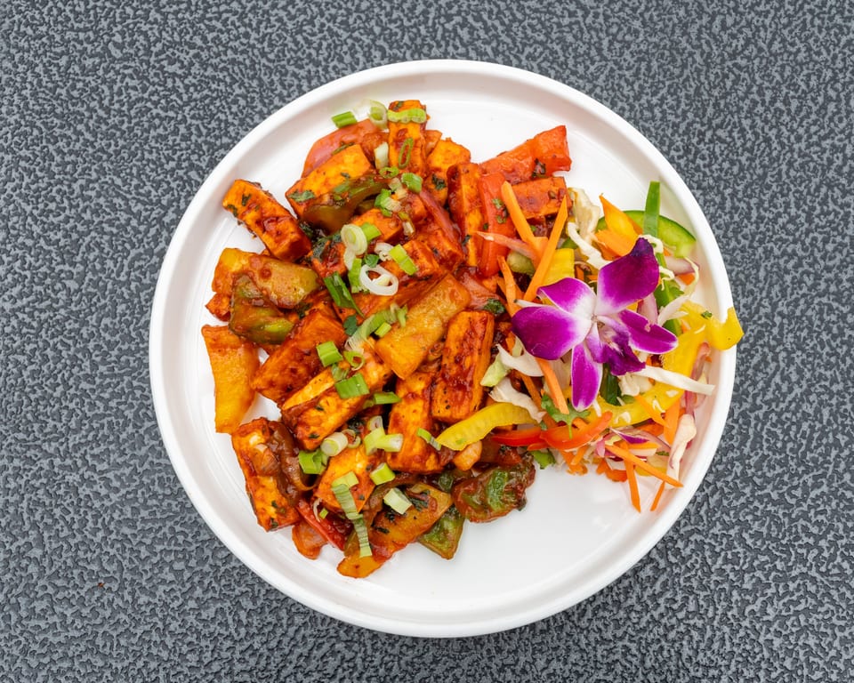 Chili Paneer with bell peppers, onions, and scallions, garnished with a side salad and orchid.