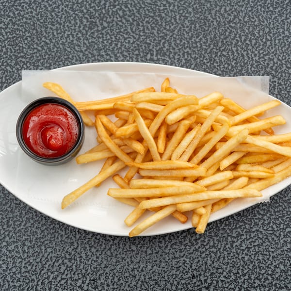 A white oval plate holds golden french fries with a side of ketchup on a dark textured surface.