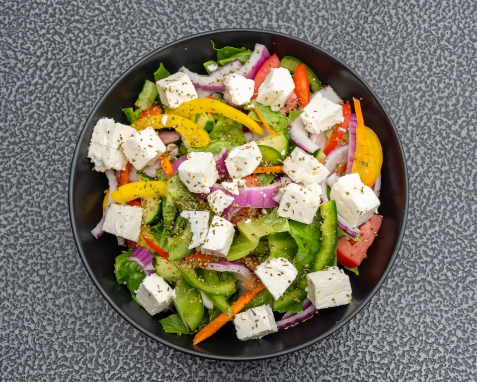 Overhead view of a colorful Greek salad with feta cheese, bell peppers, onions, and lettuce.