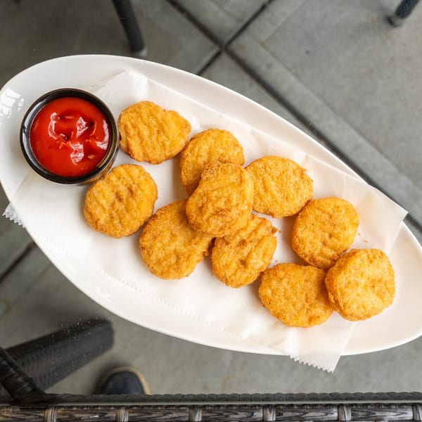 Golden-brown chicken nuggets with a side of ketchup on a white plate, viewed from above.