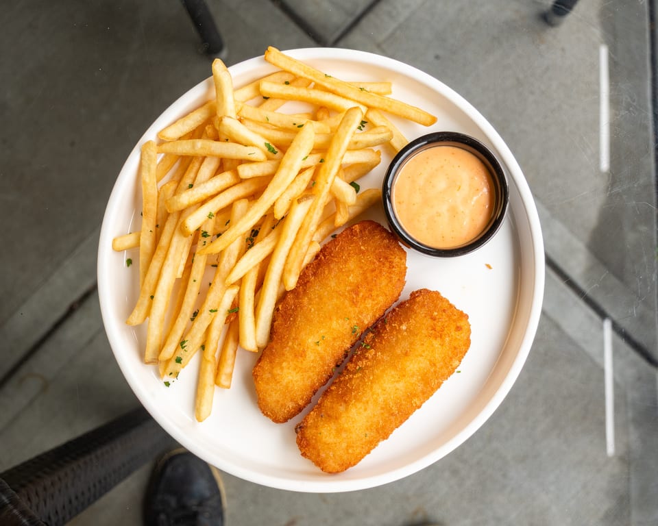 Crispy fish and chips with a side of dipping sauce on a white plate.