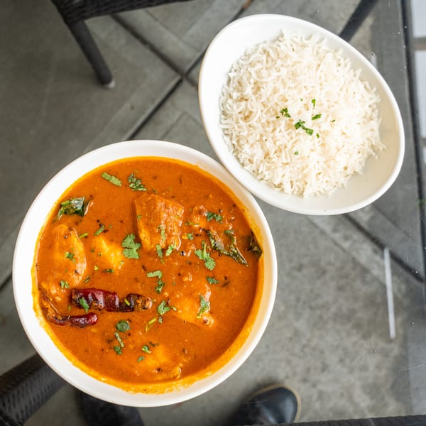 Overhead view of a bowl of orange curry with cilantro and dried chilies, next to a bowl of white rice.