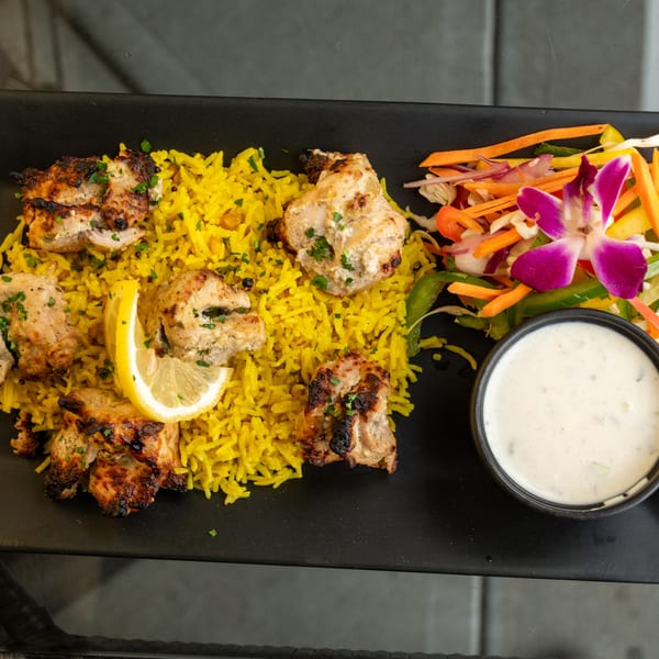 Chicken tikka with yellow rice, a side salad garnished with an orchid, and a dipping sauce.