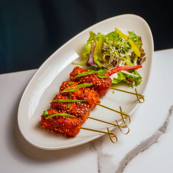 Four chicken skewers with sesame seeds and green onions, served with a side salad.