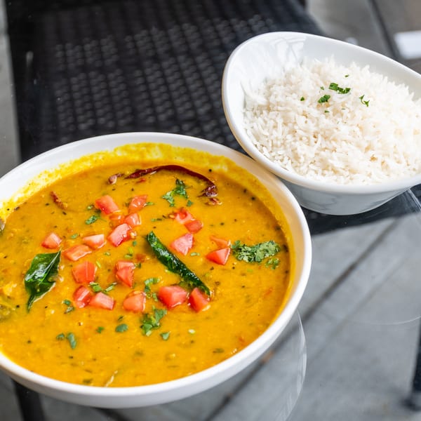 A bowl of yellow lentil dal with tomatoes and herbs, alongside a bowl of white rice.