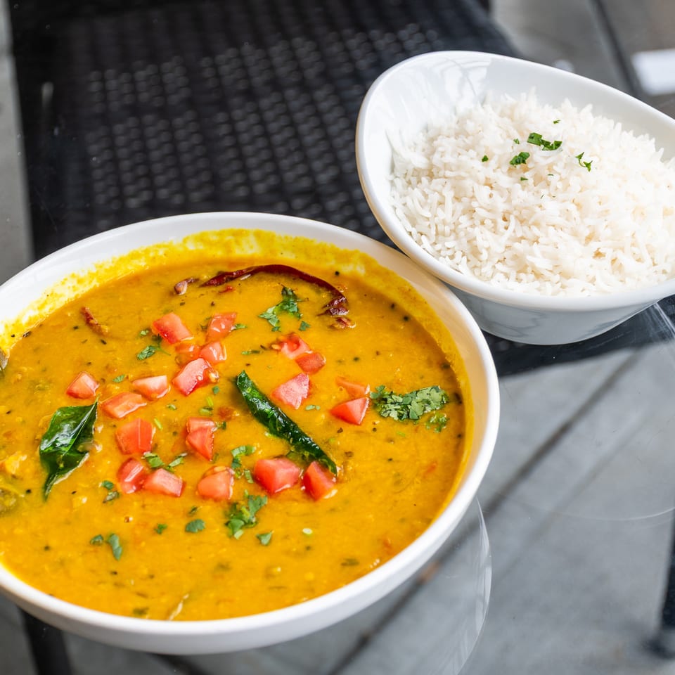 A bowl of yellow lentil dal with tomatoes and herbs, alongside a bowl of white rice.