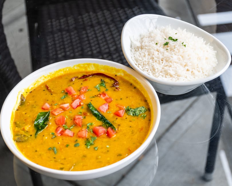A bowl of yellow lentil dal with tomatoes and herbs, alongside a bowl of white rice.