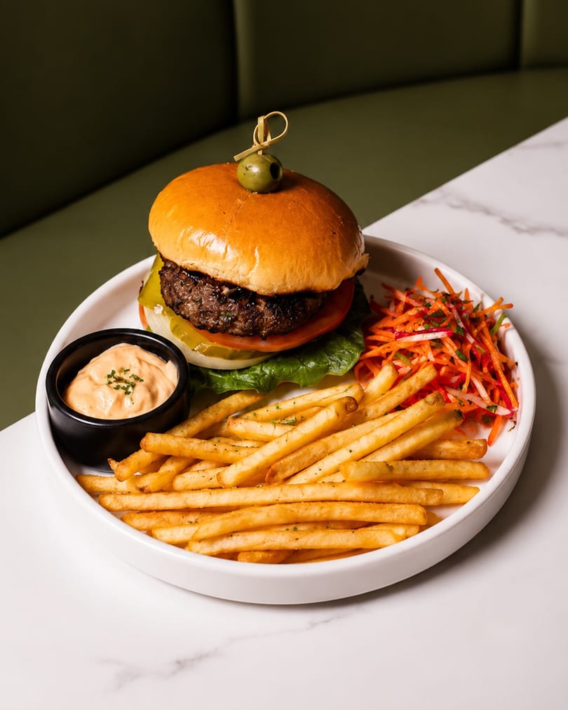 Gourmet burger with fries, dipping sauce, and a side salad on a white plate.