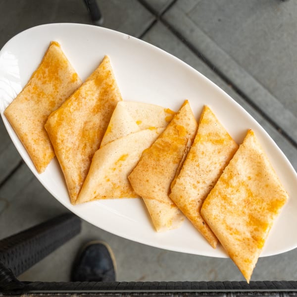 A white platter holds several triangular, golden-brown crepes, possibly filled with cheese, on a glass table.