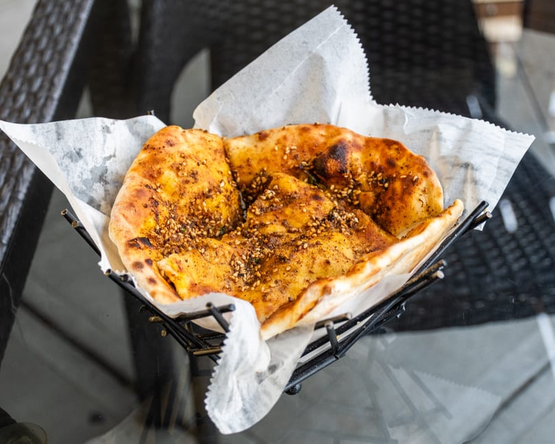 Golden brown flatbread with sesame seeds and spices, served in a black wire basket lined with parchment paper.