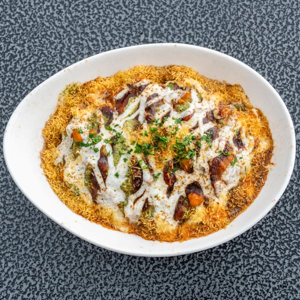 Overhead view of a white bowl filled with Indian chaat, topped with sauces and herbs.