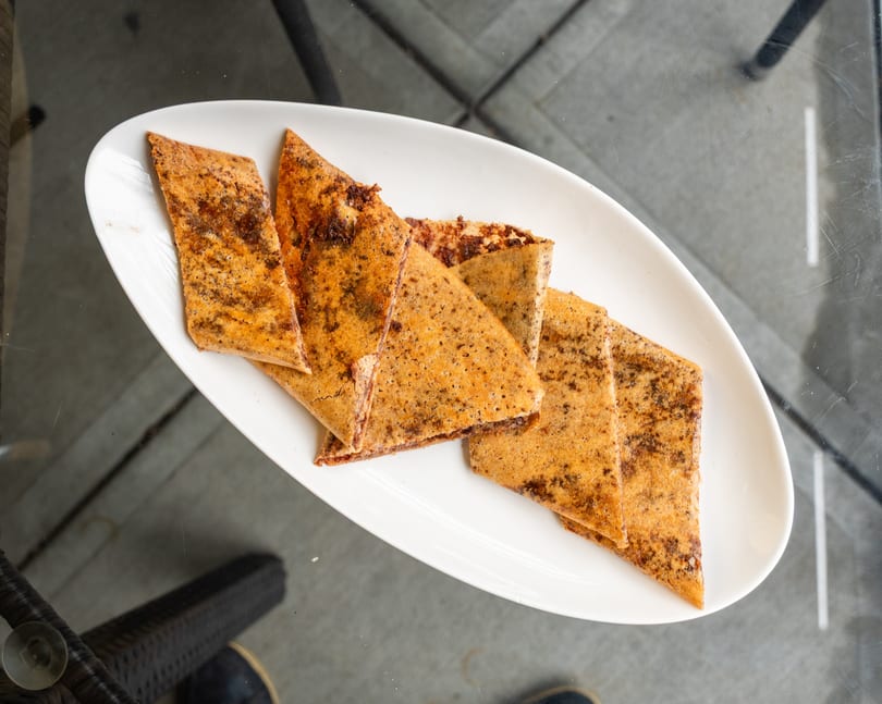 A white oval plate holds several triangular pieces of golden-brown dessert crepes with dark specks.