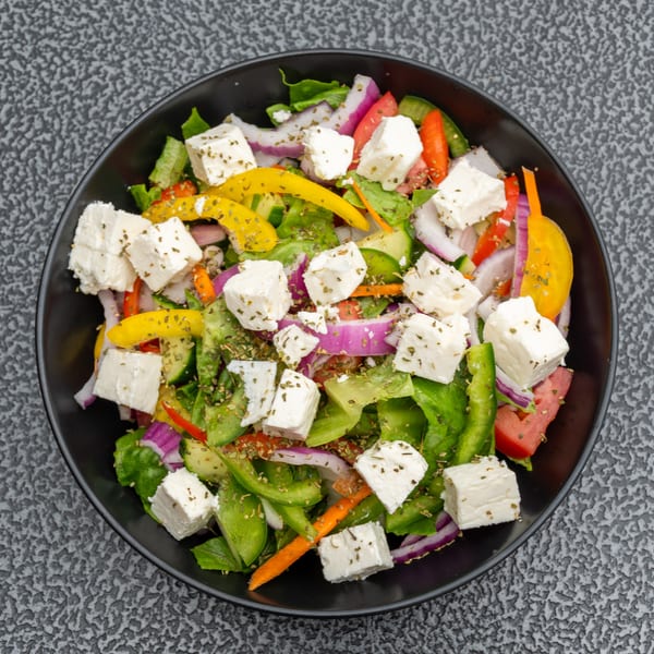 Overhead view of a vibrant Greek salad with feta, bell peppers, red onion, and lettuce in a black bowl.