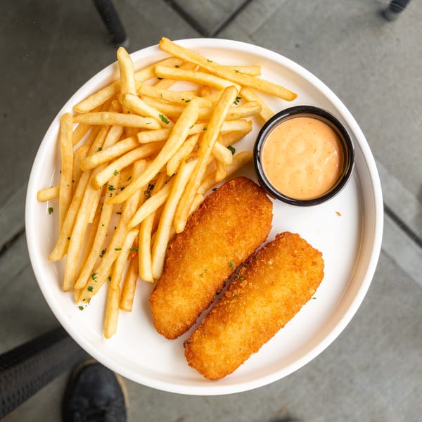 Crispy fish and chips with a side of dipping sauce on a white plate.