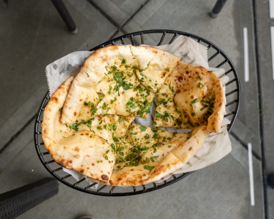 Overhead view of garlic naan bread, garnished with cilantro, in a black wire basket.